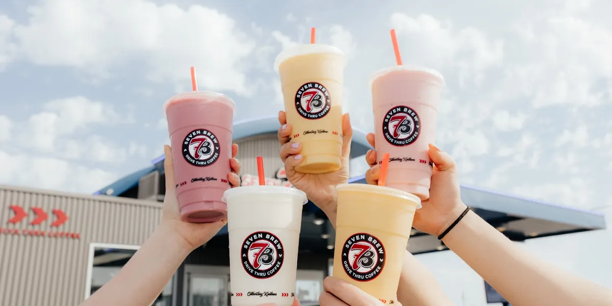 Compact drive-thru coffee stand with dual ordering lanes, outdoor seating area, and tablet-wielding baristas serving...