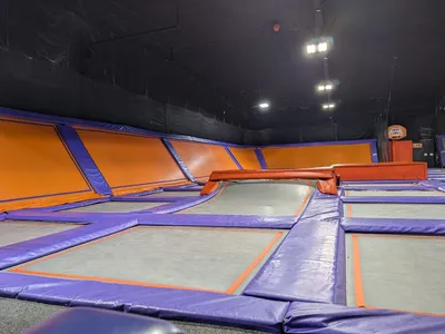Expansive indoor trampoline facility with wall-to-wall jumping surfaces, foam pits, and dedicated party areas filled with...