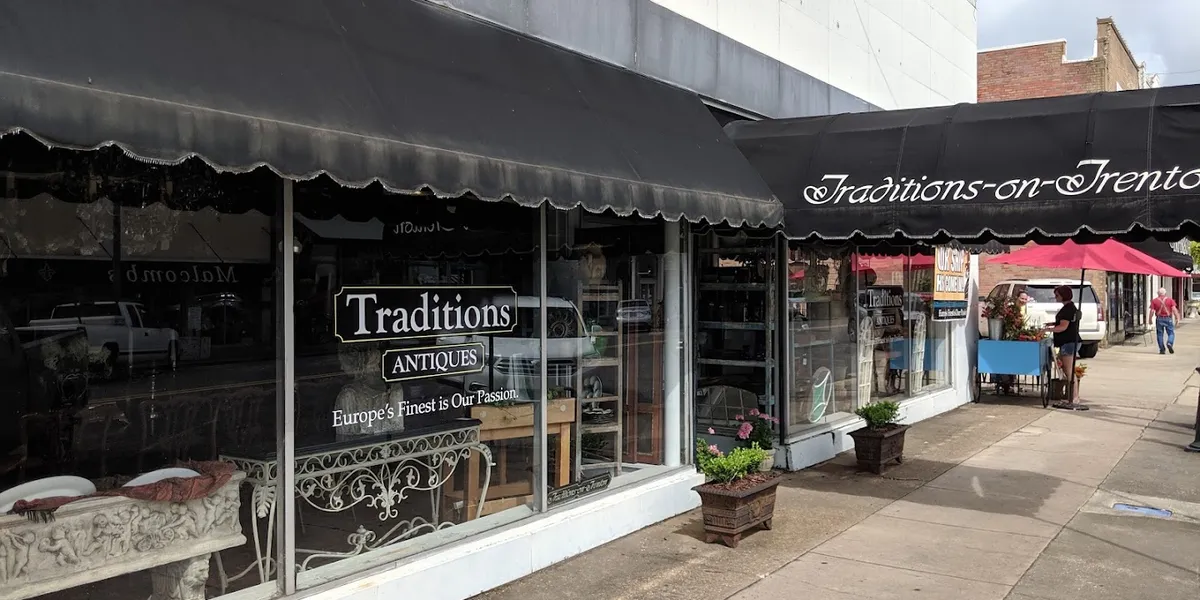 Charming row of storefronts along Trenton Street with pedestrians browsing shops, occasional street musicians, and...