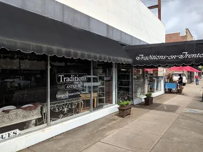 Charming row of storefronts along Trenton Street with pedestrians browsing shops, occasional street musicians, and...