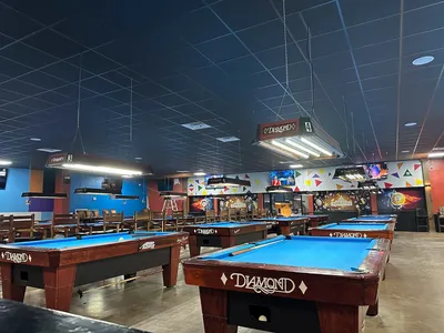 Spacious interior of Arena Billiards Bar & Grill with numerous pool tables, bar seating, and entertainment space for live...