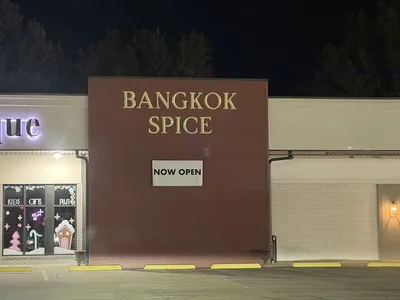 Renovated Thai restaurant interior with original booth seating, dark lighting, and traditional table settings in a quiet...