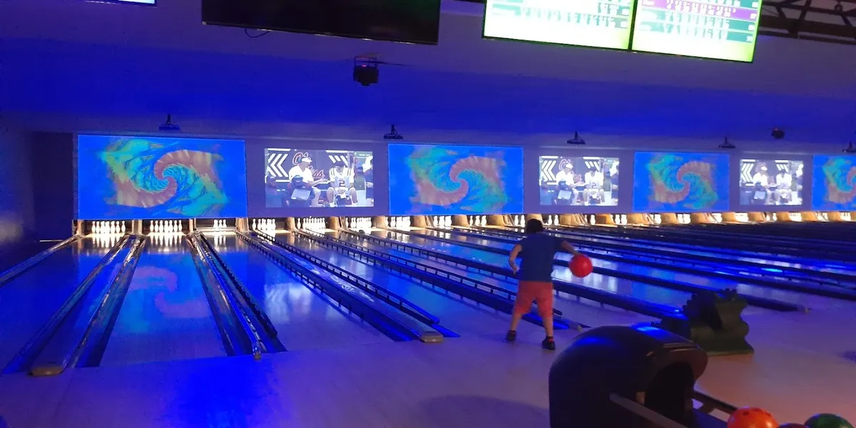 Freshly renovated bowling lanes with bright lighting and arcade games visible in the background, filled with families...
