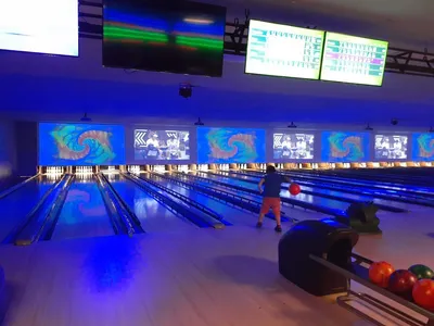 Freshly renovated bowling lanes with bright lighting and arcade games visible in the background, filled with families...