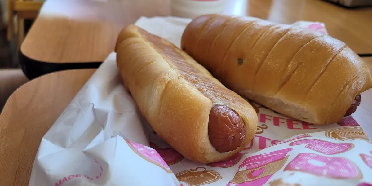 Compact donut shop counter with display case of glazed donuts and breakfast croissants, 'Hot Now' sign visible, casual...