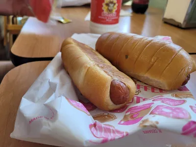 Compact donut shop counter with display case of glazed donuts and breakfast croissants, 'Hot Now' sign visible, casual...