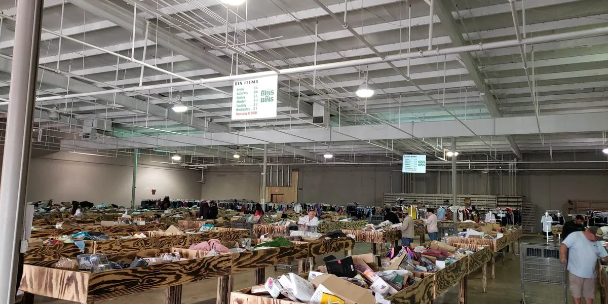 Spacious warehouse-style discount store with rows of large merchandise bins where shoppers dig for unexpected bargains on...