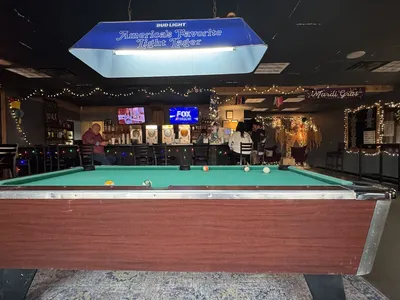 Casual daiquiri bar with pool tables, dart boards and cornhole games visible inside, featuring a busy drive-thru window...