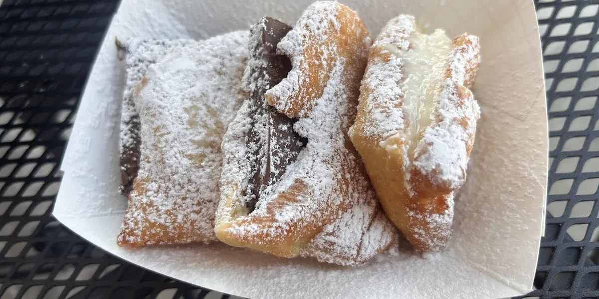 Cozy bakery with outdoor seating in Antique Alley featuring display cases of fresh croissants, beignets, and artisanal...