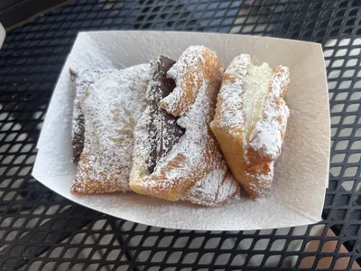 Cozy bakery with outdoor seating in Antique Alley featuring display cases of fresh croissants, beignets, and artisanal...