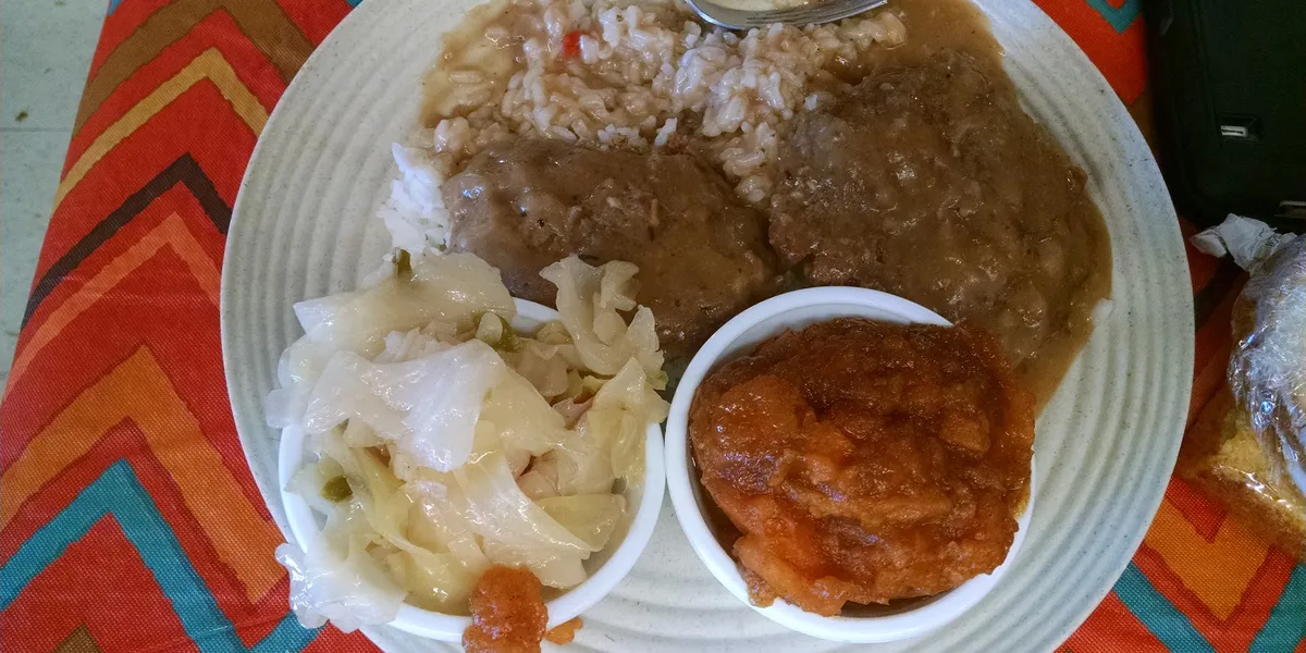Cafeteria-style soul food counter with steaming trays of smothered gar, pig feet, and candied yams in a casual, no-frills...