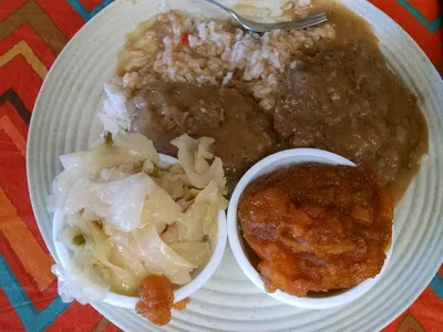 Cafeteria-style soul food counter with steaming trays of smothered gar, pig feet, and candied yams in a casual, no-frills...
