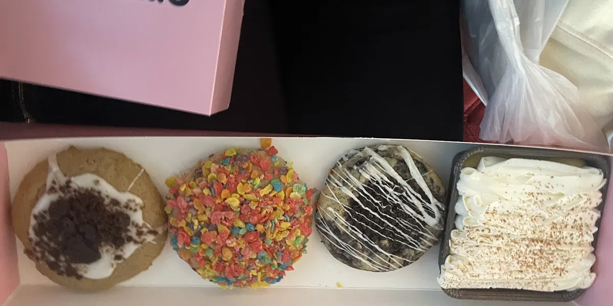 Bright, modern cookie shop with display case showcasing oversized, freshly-baked specialty cookies in Crumbl's signature...