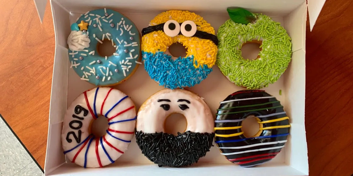 Bright donut shop with outward-facing counter seating, colorful booth area, and display case showcasing specialty cronuts...