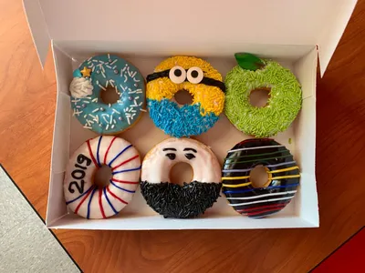 Bright donut shop with outward-facing counter seating, colorful booth area, and display case showcasing specialty cronuts...