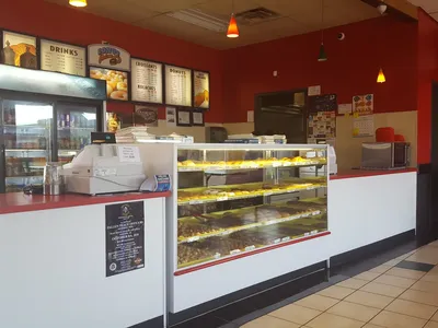 Bright donut shop counter displaying fresh-made Texas-style pastries, featuring boudin kolaches and chocolate glazed...