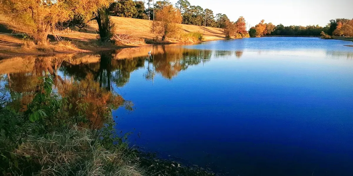 Scenic riverside recreation area with walking paths, picnic tables, and boat ramp overlooking the Ouachita River at sunset.