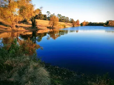 Scenic riverside recreation area with walking paths, picnic tables, and boat ramp overlooking the Ouachita River at sunset.