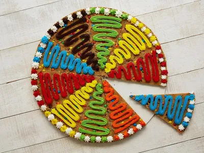 Glass counter displaying colorfully decorated cookies and custom cookie cakes with detailed designs in a bright mall...