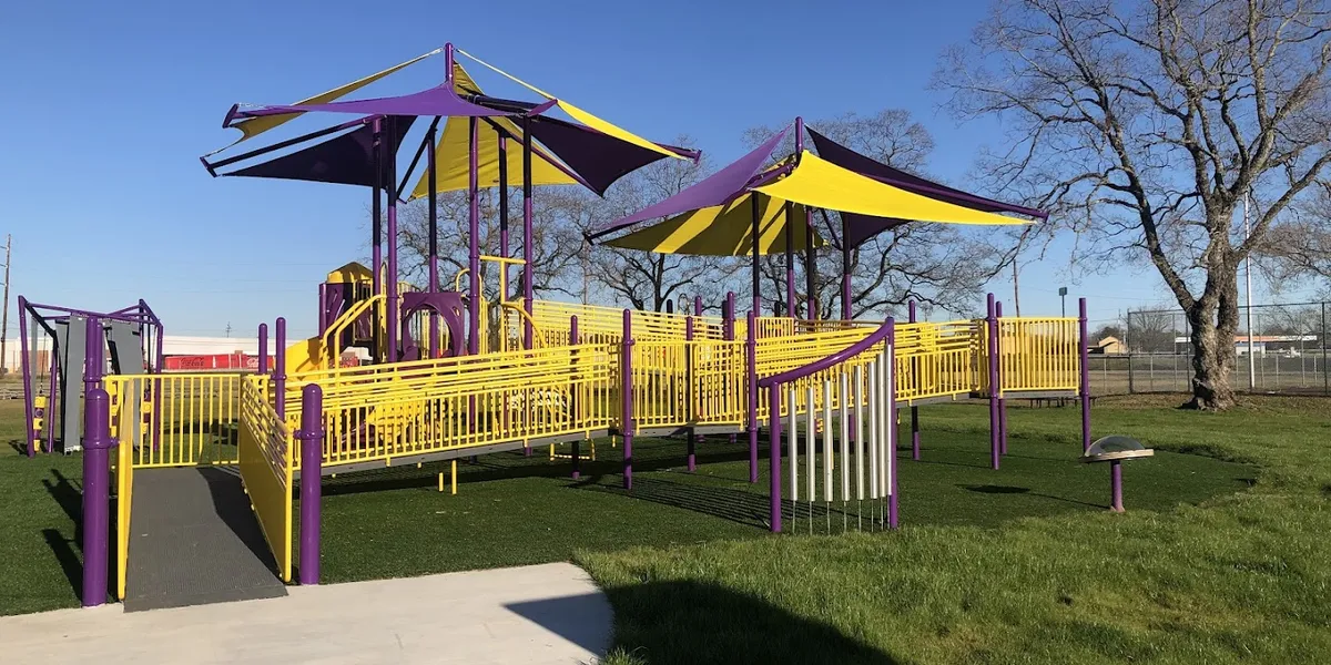 Spacious community center with modern all-inclusive playground featuring colorful turf surfaces, slides, and activity...