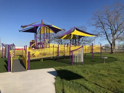 Spacious community center with modern all-inclusive playground featuring colorful turf surfaces, slides, and activity...