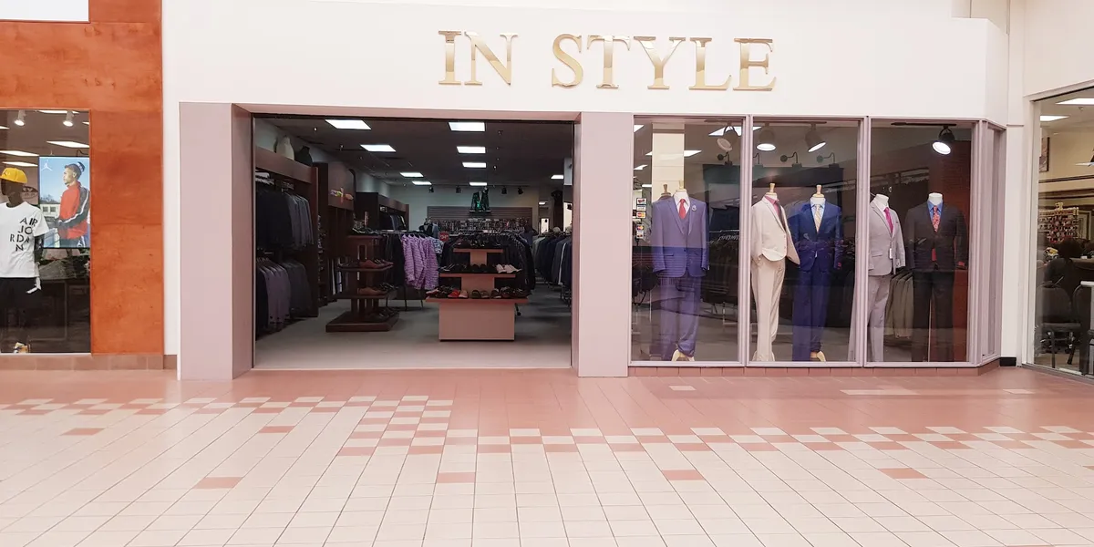 Intimate men's clothing store with dimmed lighting showcasing racks of distinctive suits and formal wear in a compact...