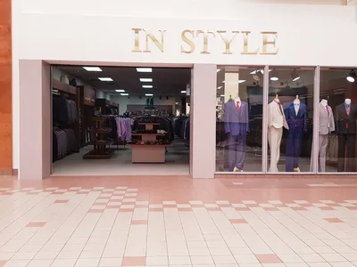 Intimate men's clothing store with dimmed lighting showcasing racks of distinctive suits and formal wear in a compact...