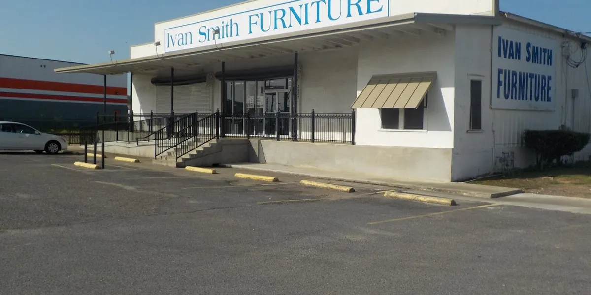 Spacious furniture showroom with organized displays of living room, bedroom, and dining sets under bright lighting with...