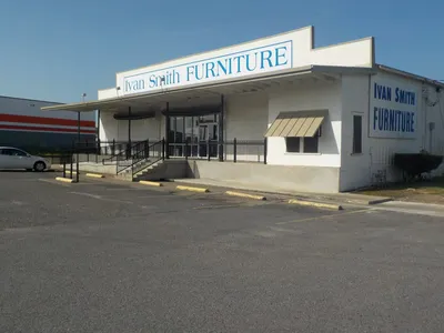 Spacious furniture showroom with organized displays of living room, bedroom, and dining sets under bright lighting with...