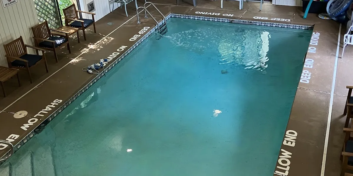 Spacious indoor swimming pool with adjacent hot tub, surrounded by pool chairs and colorful floaties in a private,...