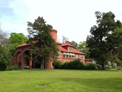 Stately 19th-century southern mansion with sprawling grounds, ancient trees, and ornate architectural details bathed in...