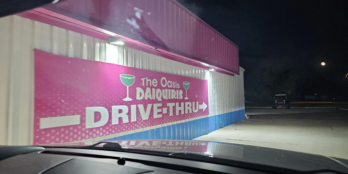 Colorful frozen daiquiris in to-go cups with names like 'Skittles' and 'Kiss of Death' displayed at Oasis Daiquiris'...