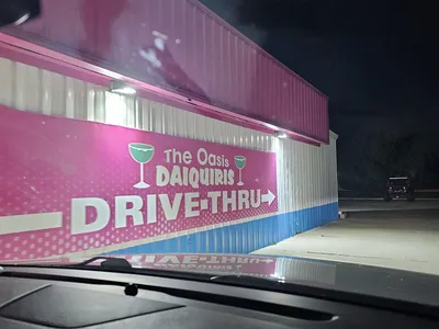 Colorful frozen daiquiris in to-go cups with names like 'Skittles' and 'Kiss of Death' displayed at Oasis Daiquiris'...