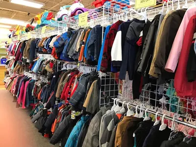 Neatly organized racks of children's secondhand clothing in a bright, clean retail space with clearly marked sections by...