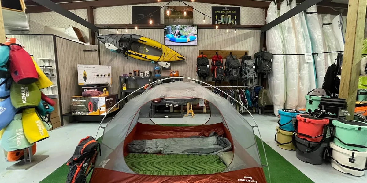 Specialized paddle shop with kayaks and SUPs displayed throughout, featuring outdoor gear and a community bulletin board...