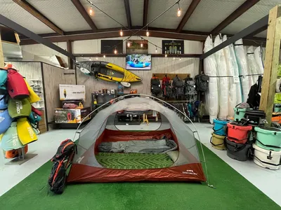 Specialized paddle shop with kayaks and SUPs displayed throughout, featuring outdoor gear and a community bulletin board...