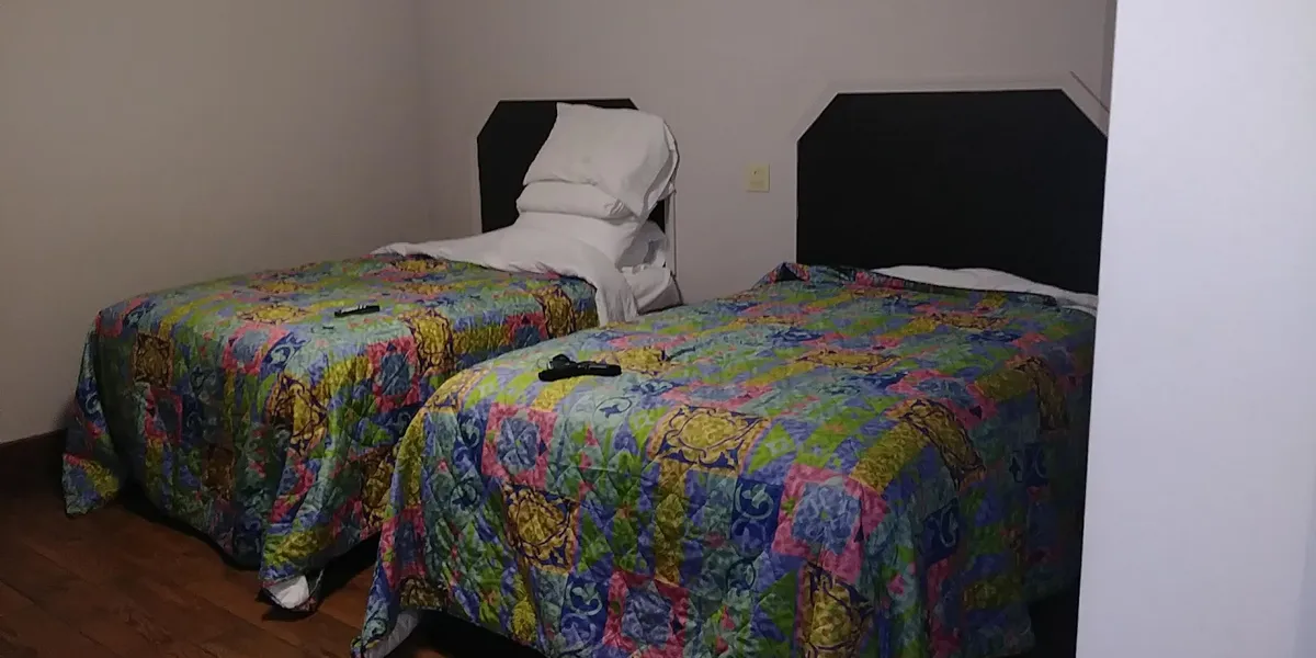 Modest roadside motel with parking lot along Louisville Ave, featuring simple exterior with row of numbered doors and...