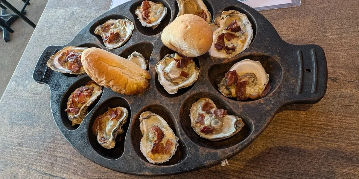 Rustic gastropub with river-view balcony, high-top seating, and vintage bar rail overlooking the Ouachita River at sunset.