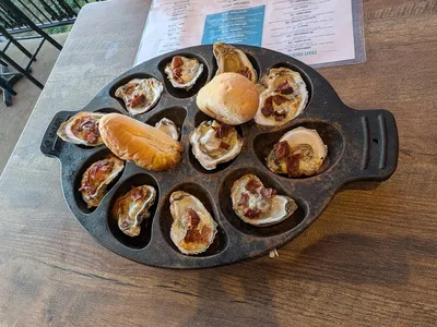 Rustic gastropub with river-view balcony, high-top seating, and vintage bar rail overlooking the Ouachita River at sunset.