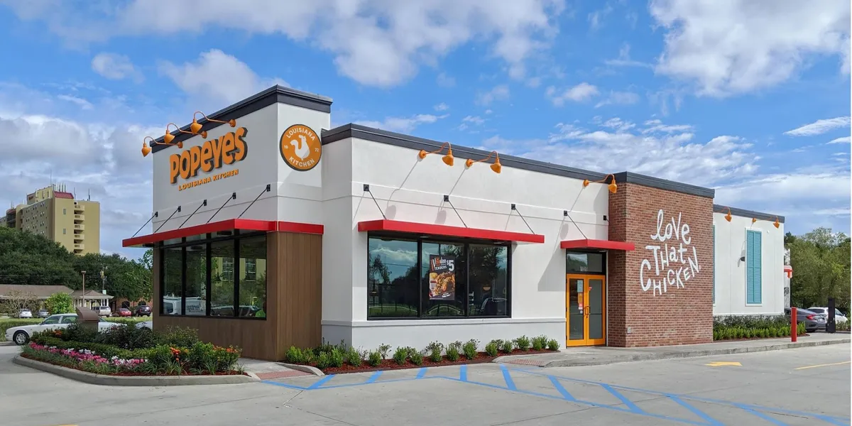 Popeyes Louisiana Kitchen storefront on Louisville Ave with outdoor seating area, drive-thru lane, and red-and-orange...
