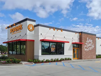 Popeyes Louisiana Kitchen storefront on Louisville Ave with outdoor seating area, drive-thru lane, and red-and-orange...