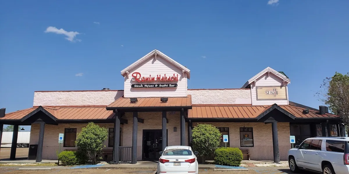 Bustling hibachi grill station with chefs preparing meals alongside a separate sushi bar where diners watch artful roll...