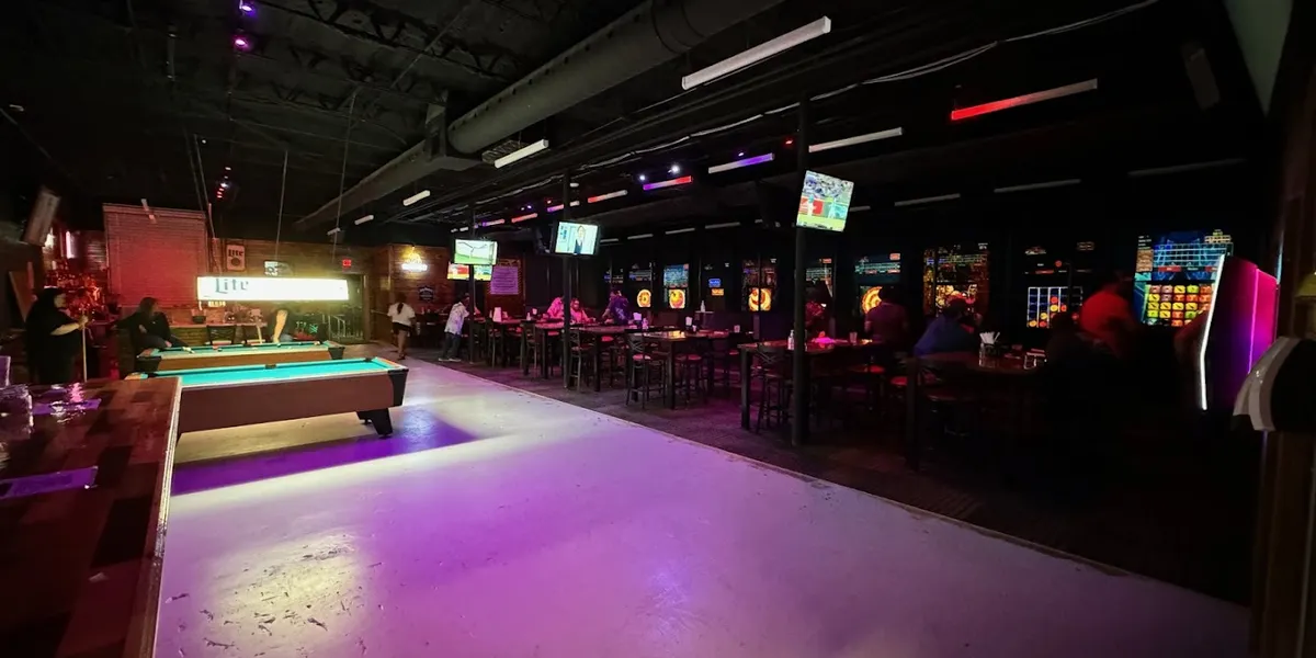 Indoor axe-throwing lanes with wooden targets alongside a bar serving craft cocktails in a spacious, lively event venue.