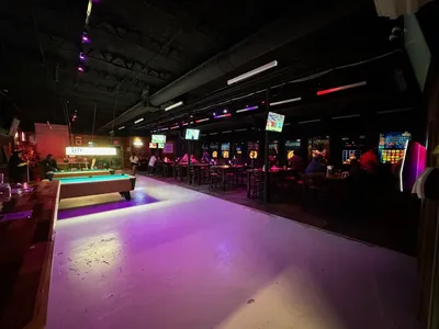 Indoor axe-throwing lanes with wooden targets alongside a bar serving craft cocktails in a spacious, lively event venue.