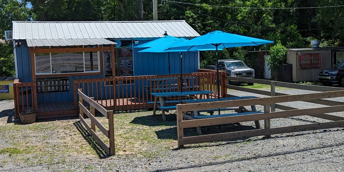 Clean ice cream shop with visible prep area, outdoor picnic tables under umbrellas, and a large menu board displaying...