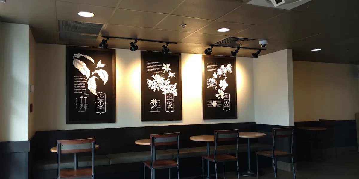 Compact Starbucks counter in ULM food court with efficient service line, outdoor tables visible through windows, and...