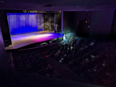 Intimate theater with new comfortable seating arranged before a well-lit stage, where local talent performs in a clean,...