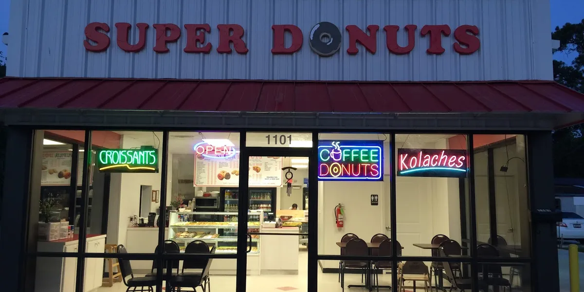 Bright, clean donut shop counter displaying fresh-made pastries with coffee station nearby, frequented by local...
