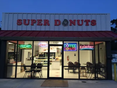 Bright, clean donut shop counter displaying fresh-made pastries with coffee station nearby, frequented by local...