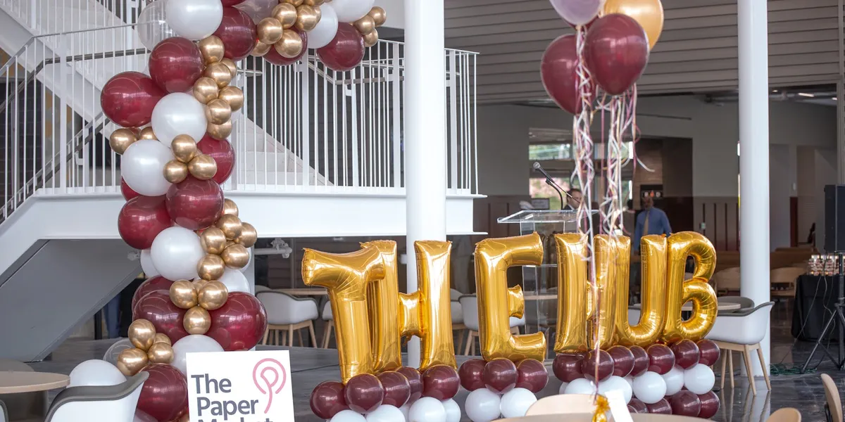 Bright, well-lit party supply store with colorful balloon displays, gift packaging options, and a central table of white...